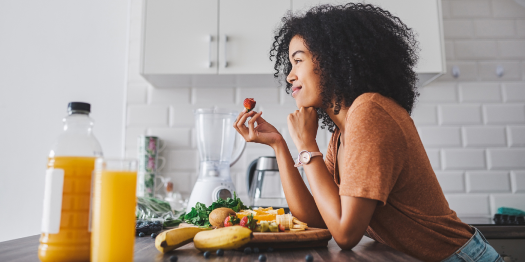 Woman eating fresh fruit and nutritious foods in a kitchen to support healthy winter habits.